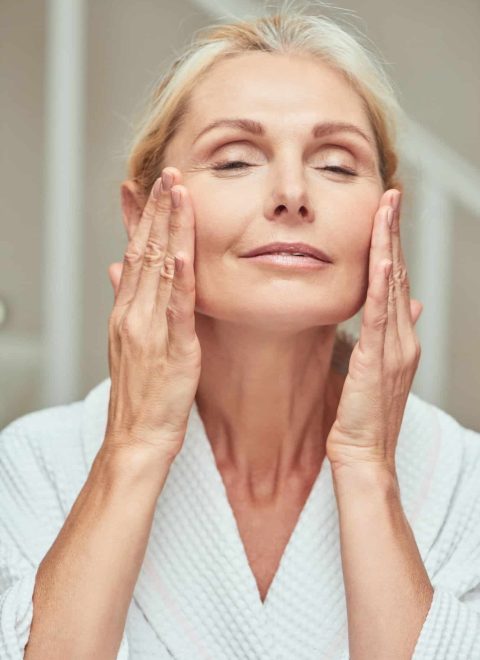 Happy middle aged caucasian woman making facial massage